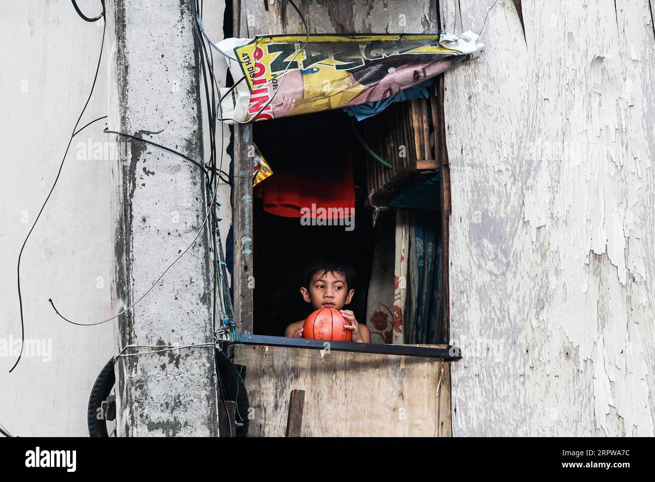 Slum Window 200424 -- BEIJING, April 24, 2020 -- A boy holds a ball as he looks out ...