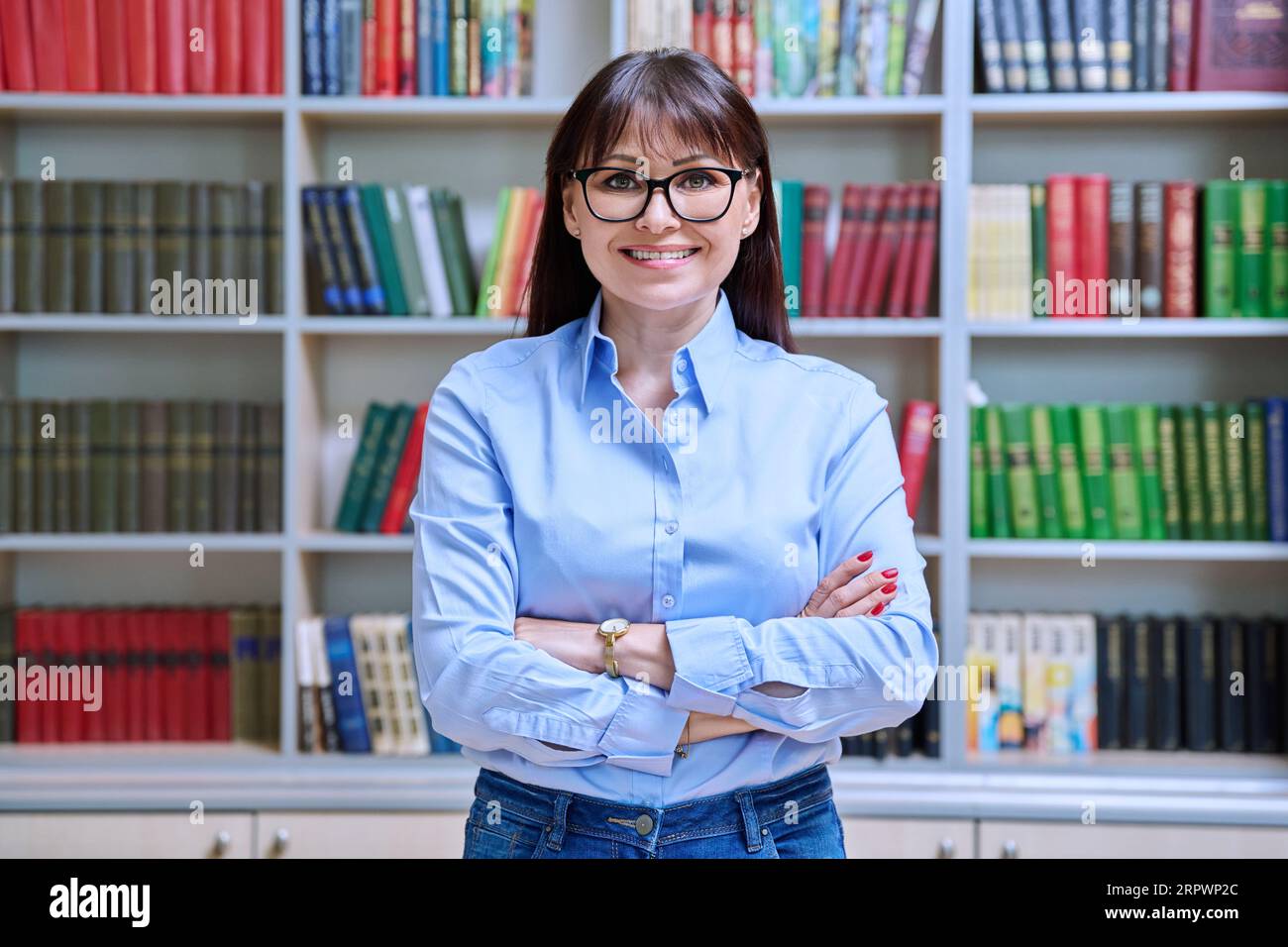 Portrait of confident female teacher with crossed arms inside library ...