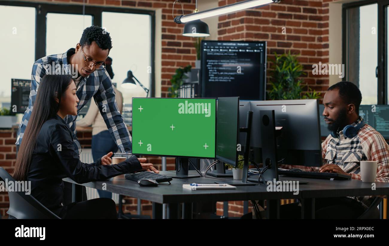 Two software developers analyzing source code looking at green screen chroma key mockup with coworker sitting at desk writing algorithm. Software developers working on artificial intelligence project. Stock Photo