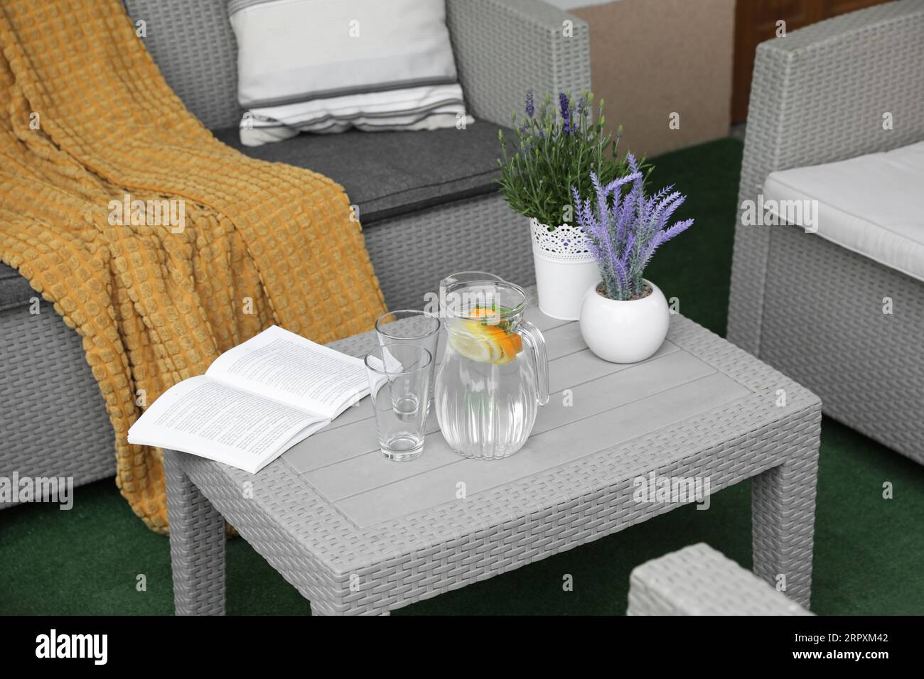 Table with book, jug of water and potted plants in front of sofa on outdoor terrace Stock Photo