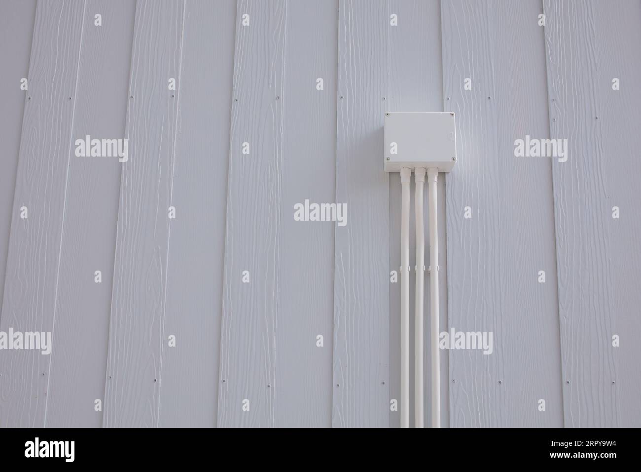 White Plastic Electrical Junction Box with Conduit Installed on the wall of a white wooden house Stock Photo