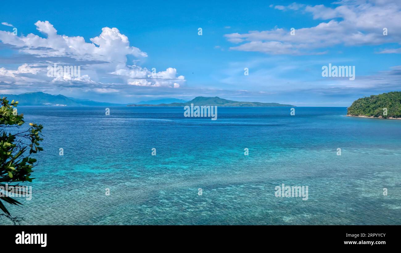 Tropical coral in shallow turquoise water in the tourist resort of Puerto Galera, Philippines, with Verde Island straight ahead and southern Luzon. Stock Photo