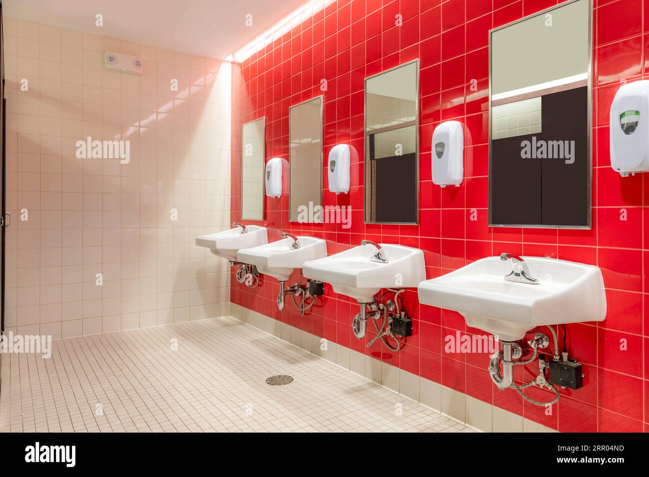 Public restroom with red tile and four, lavatories, sinks Stock Photo