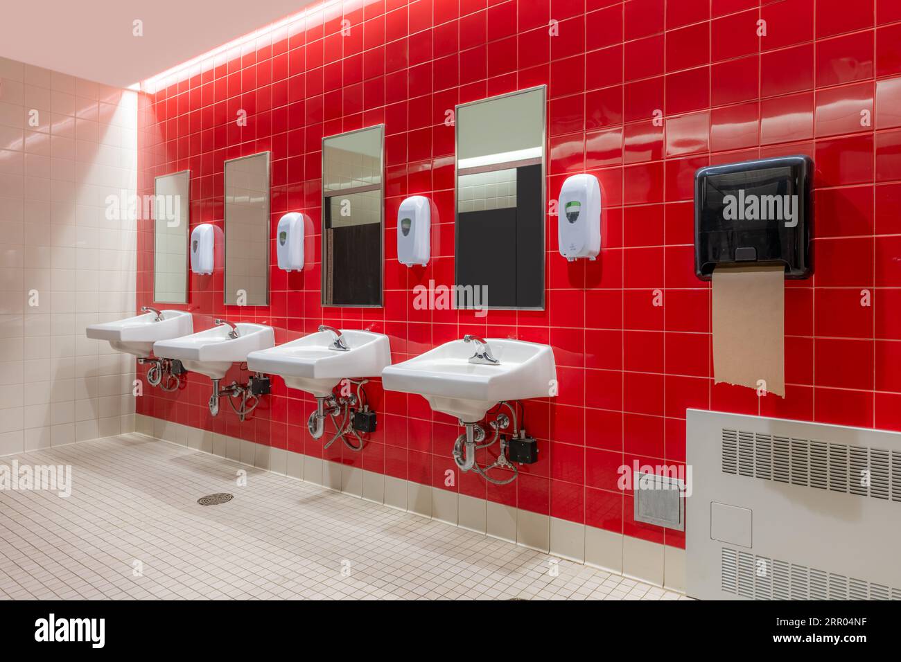 Public restroom with red tile and four, lavatories, sinks Stock Photo