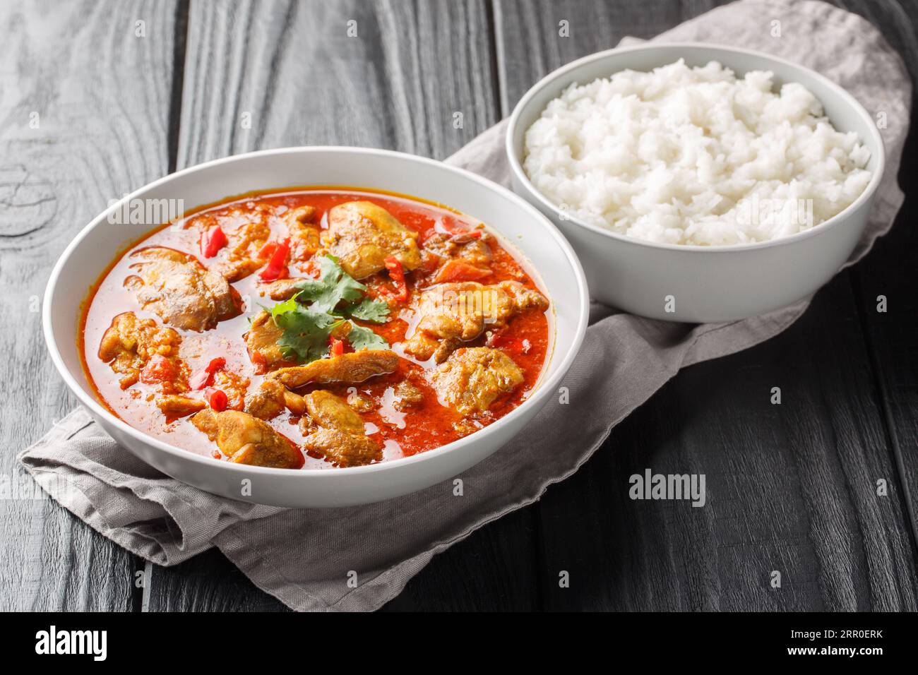 Homemade chicken curry in red spicy sauce served with jasmine rice close-up in a bowl on the table. Horizontal Stock Photo