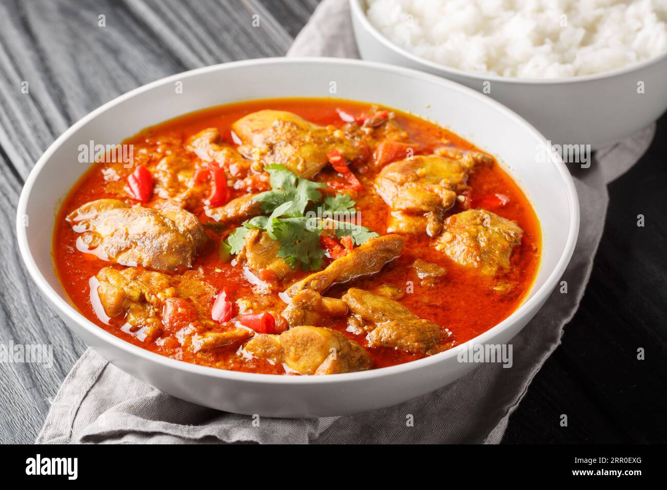 Spicy Burmese chicken curry in a sauce consisting of onion, ginger, lemongrass, pepper, garlic and tomato close-up in a bowl on the table. Horizontal Stock Photo