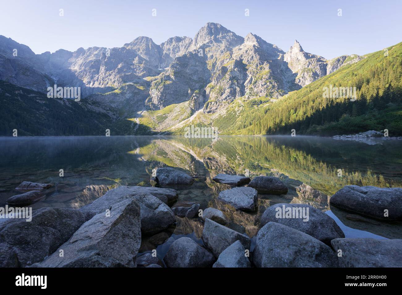 Majestic peak reflecting in pristine crystal clear alpine lake with rocky foreground, Poland, Europe Stock Photo