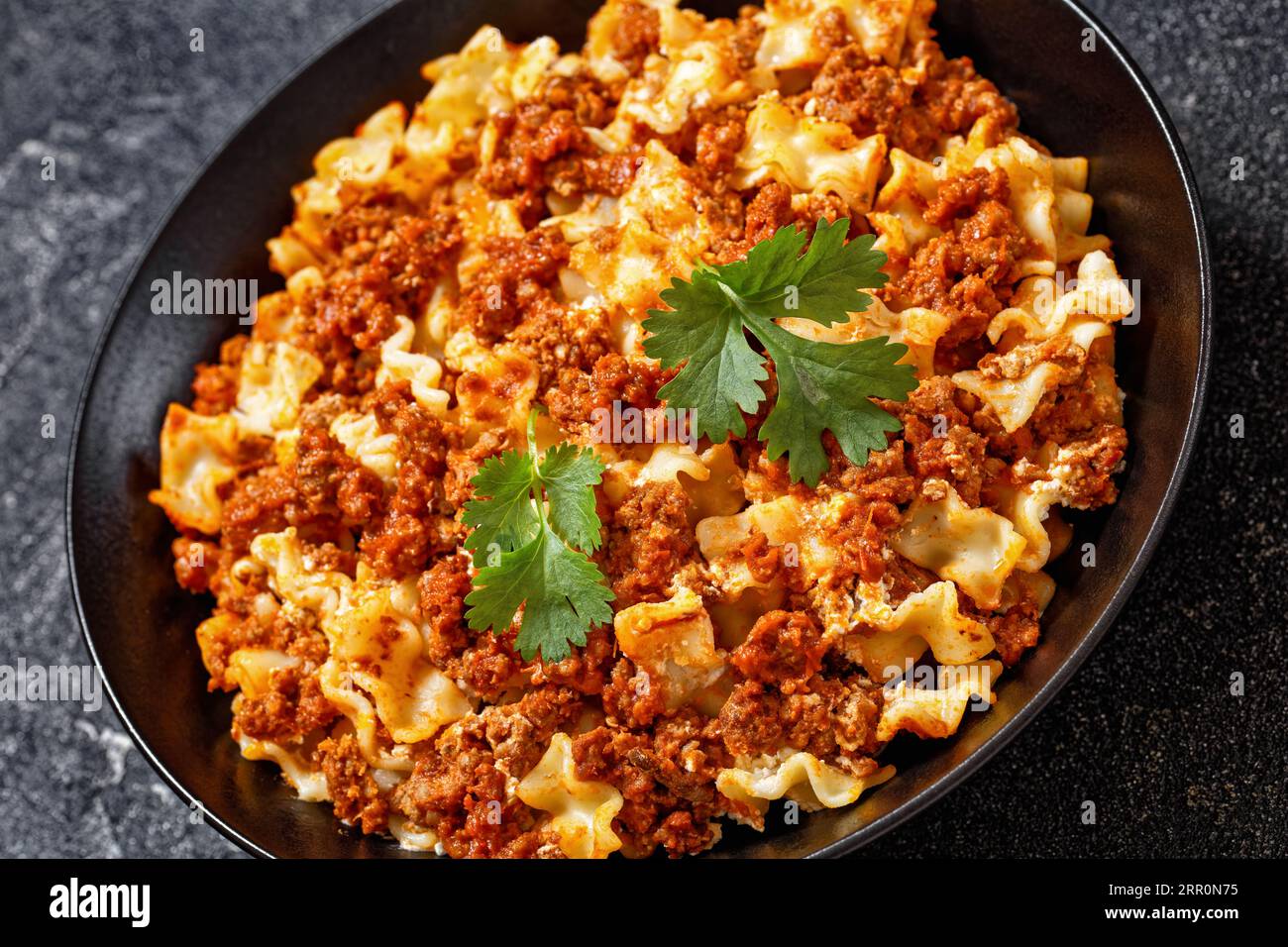 bolognese with ground beef, tomatoes, ricotta and cheese on black bowl on concrete