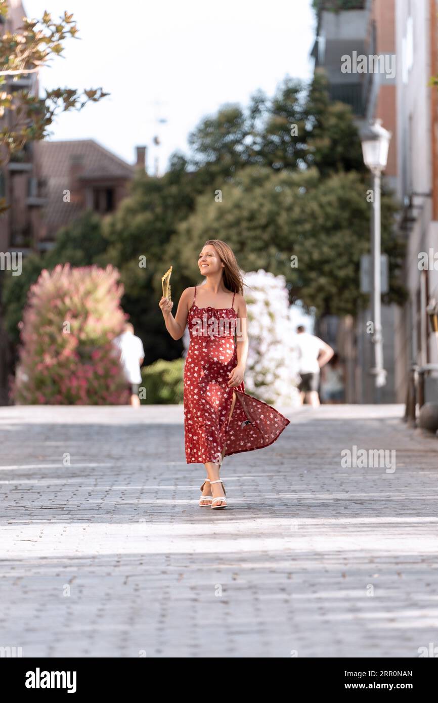 Woman in dress smiling while walking on the street with a hand fan. Summer concept. Stock Photo