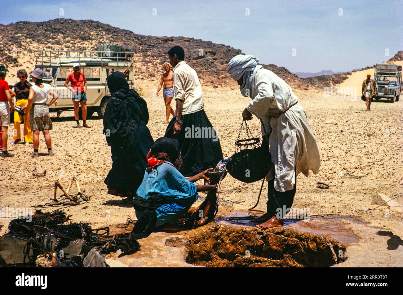 Nomads drawing water from a well, Minitrek Expeditions tourist group, near Djanet, Algeria, North Africa 1973 Stock Photo