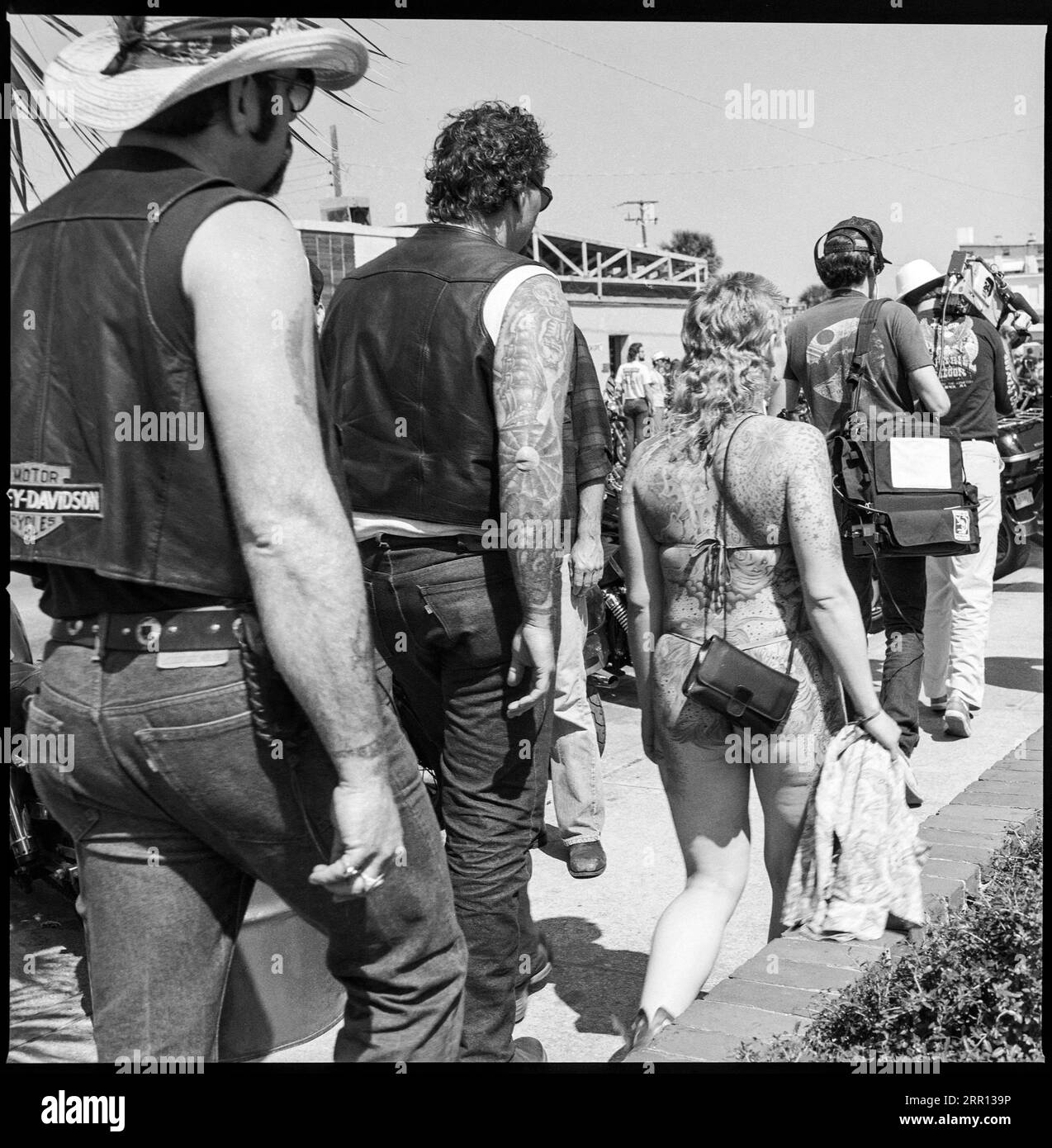 woman displays her full body tattoos walking down the street wearing a bikini in line of bikers during Daytona Bike Week in March 1986 in Daytona Beach, Florida, United States Stock Photo