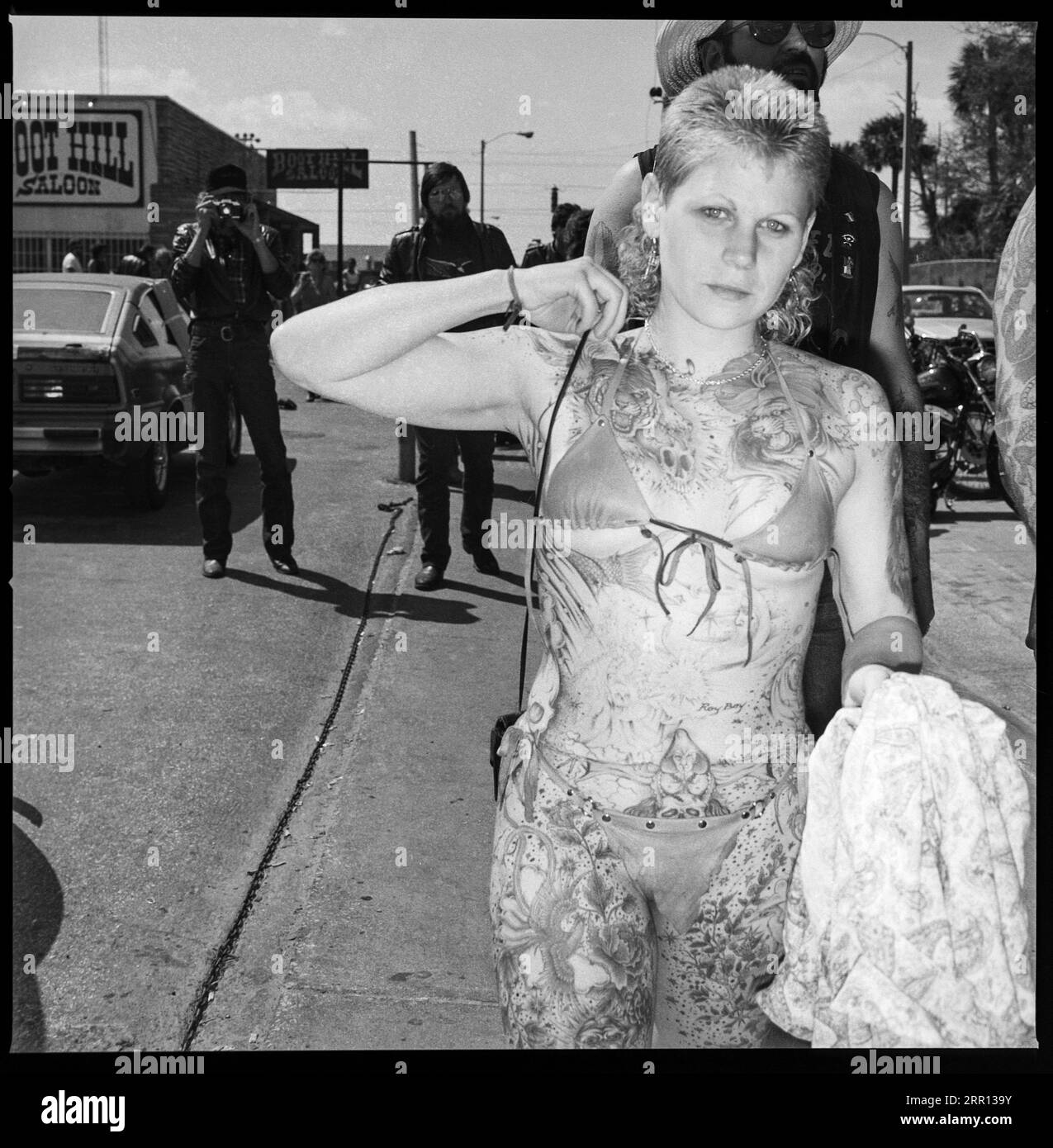 woman displays her full body tattoos walking down the street wearing a bikini during Daytona Bike Week in March 1986 in Daytona Beach, Florida, United States Stock Photo