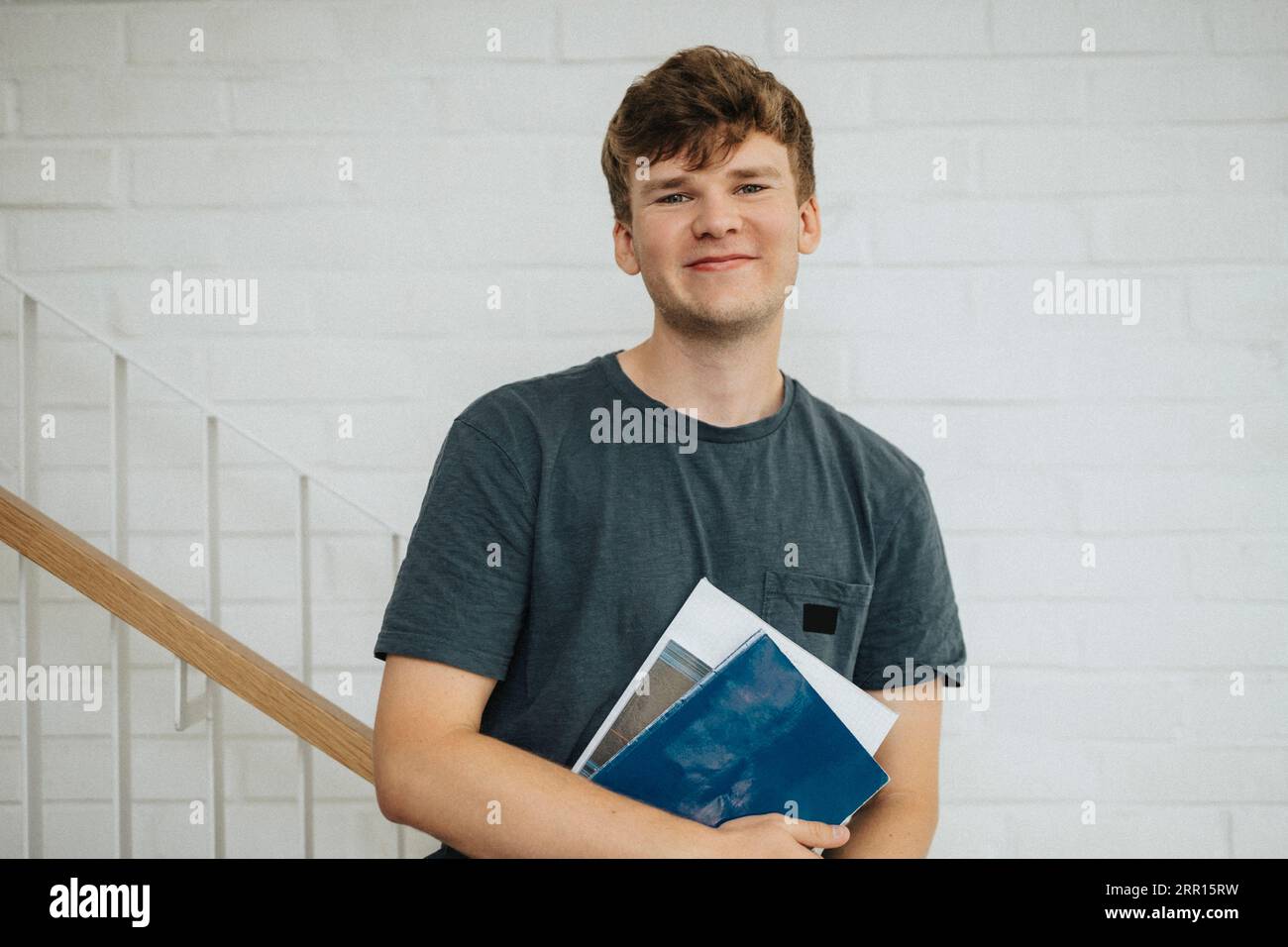 Portrait of smiling male student holding books standing in university ...