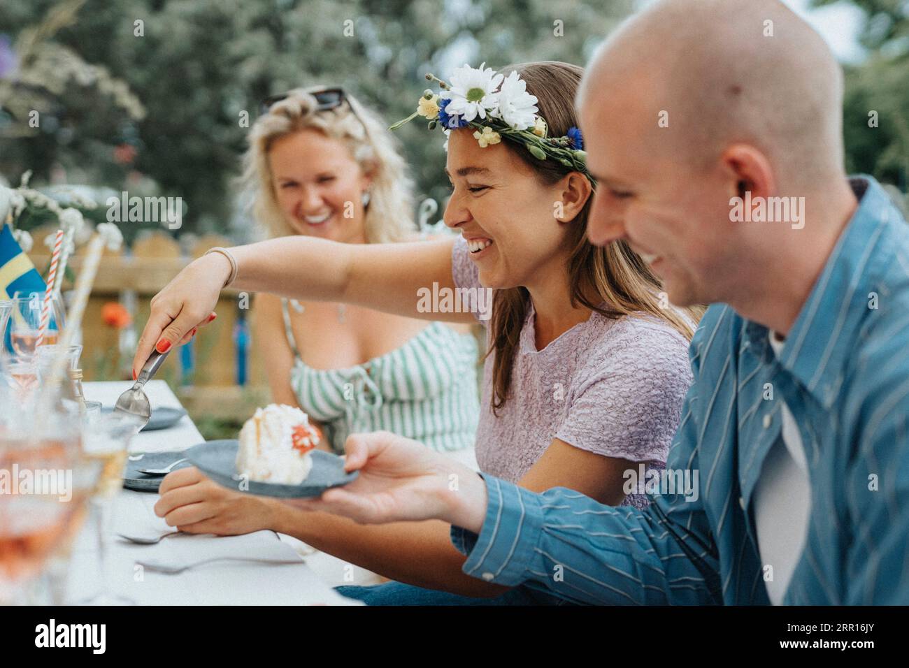 Happy young woman wearing tiara while serving cake to male friend during dinner party at cafe Stock Photo