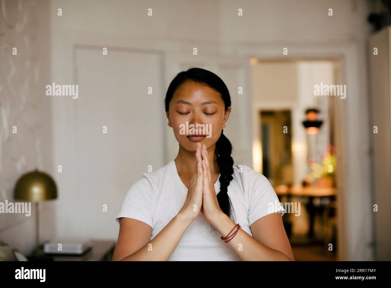 Young woman with hands clasped meditating at home Stock Photo