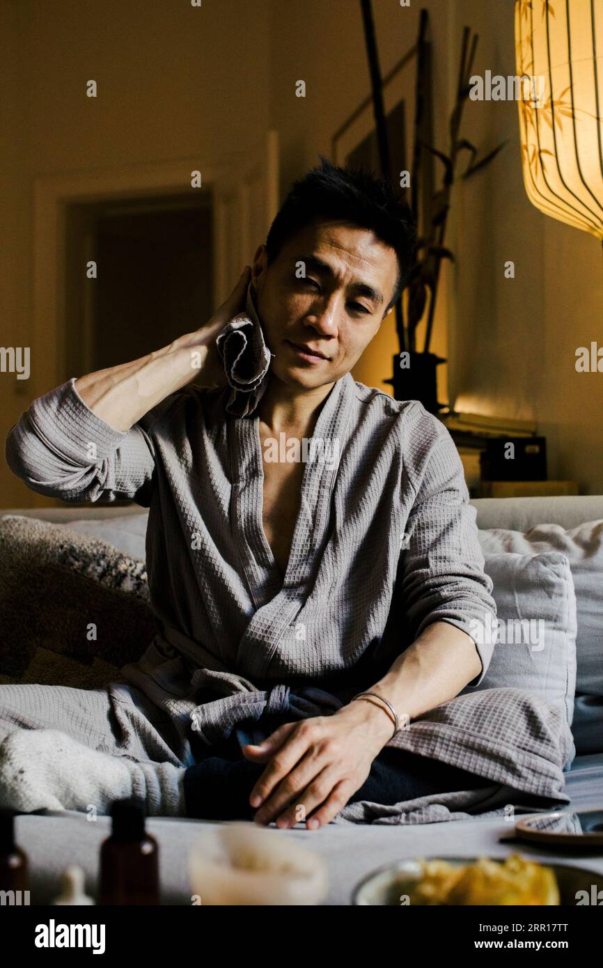 Man wiping sweat while sitting on sofa at home Stock Photo