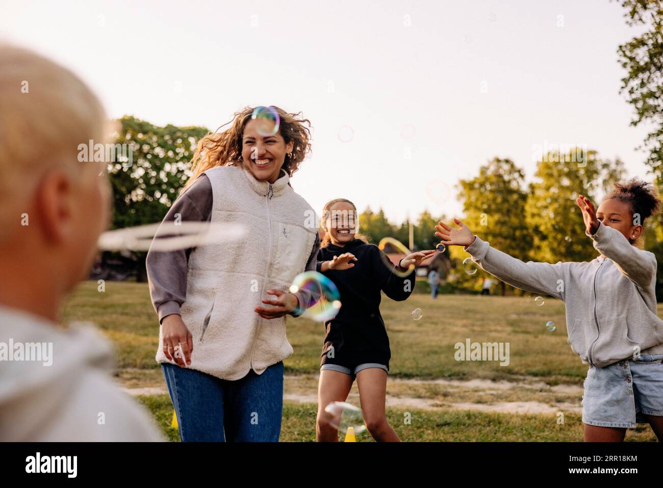 Happy children playing amidst bubbles with counselor in playground at summer camp Stock Photo