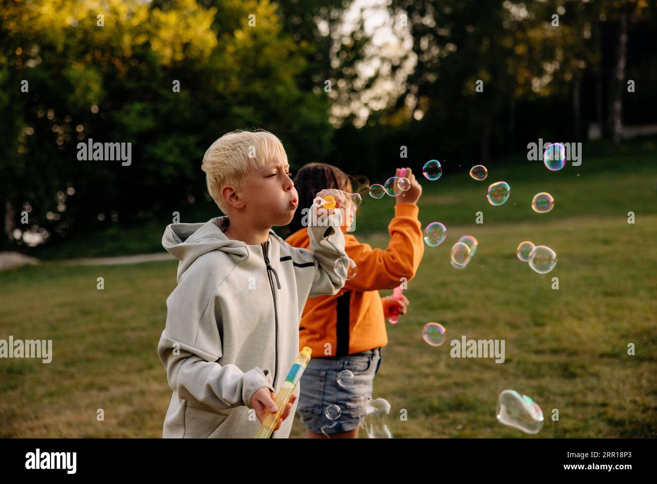 Boy blowing bubbles with female friend standing in playground at summer camp Stock Photo