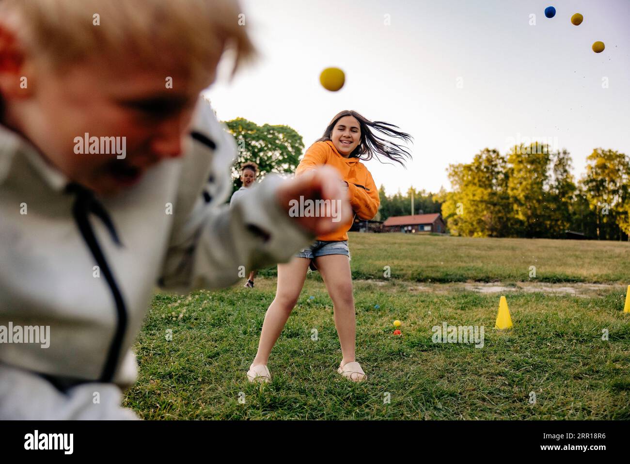 Smiling girl throwing ball on friend while playing in playground at summer camp Stock Photo