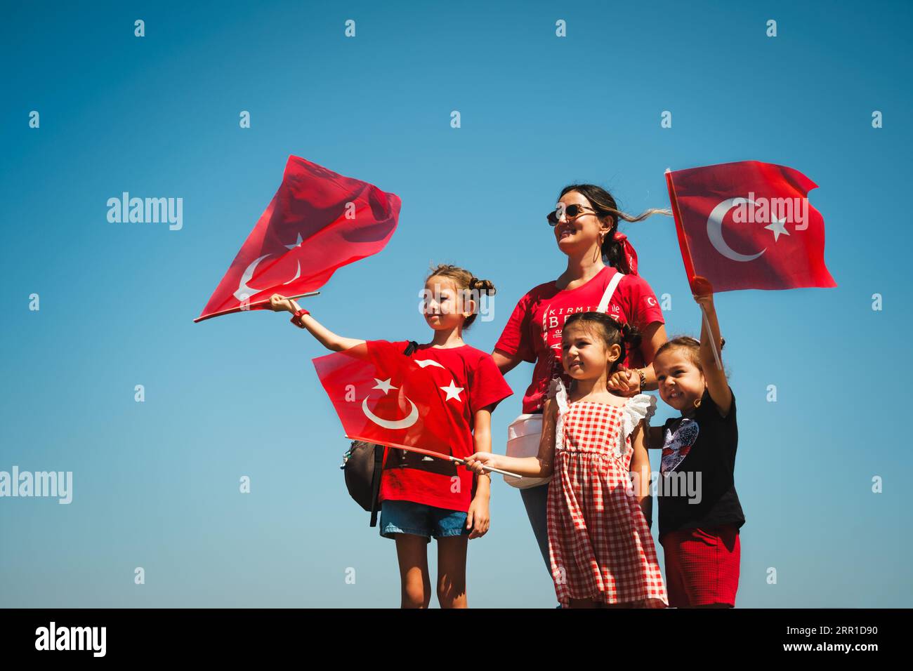 Izmir, Turkey - August 30, 2023: During Victory Day at Cumhuriyet Square, a mother and three daughters in red and flag-themed outfits wave Turkish fla Stock Photo