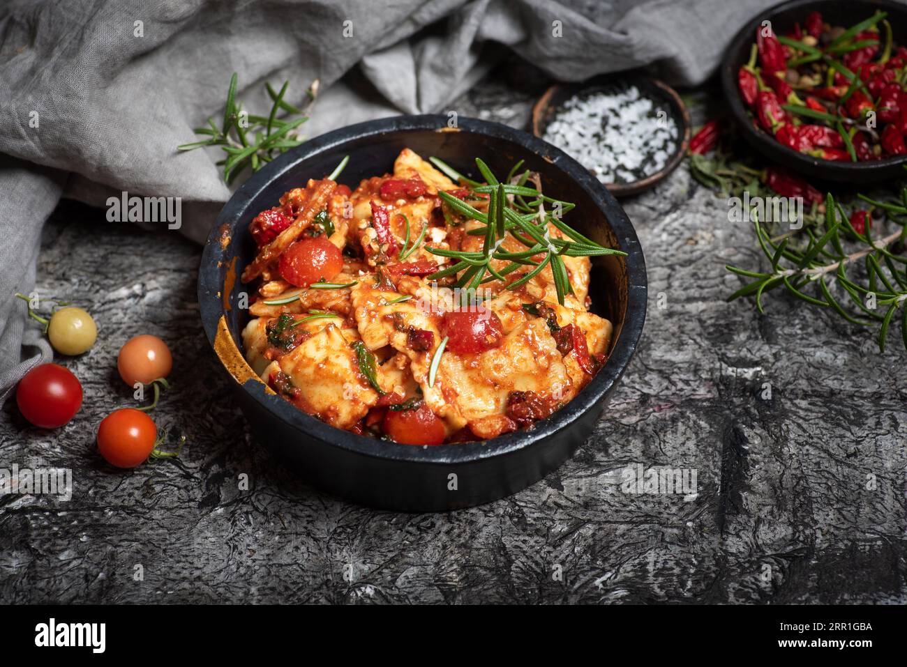 Ravioli, with cherry tomatoes, garnished with rosemary, in a black bowl on a gray wooden background. Top view Stock Photo