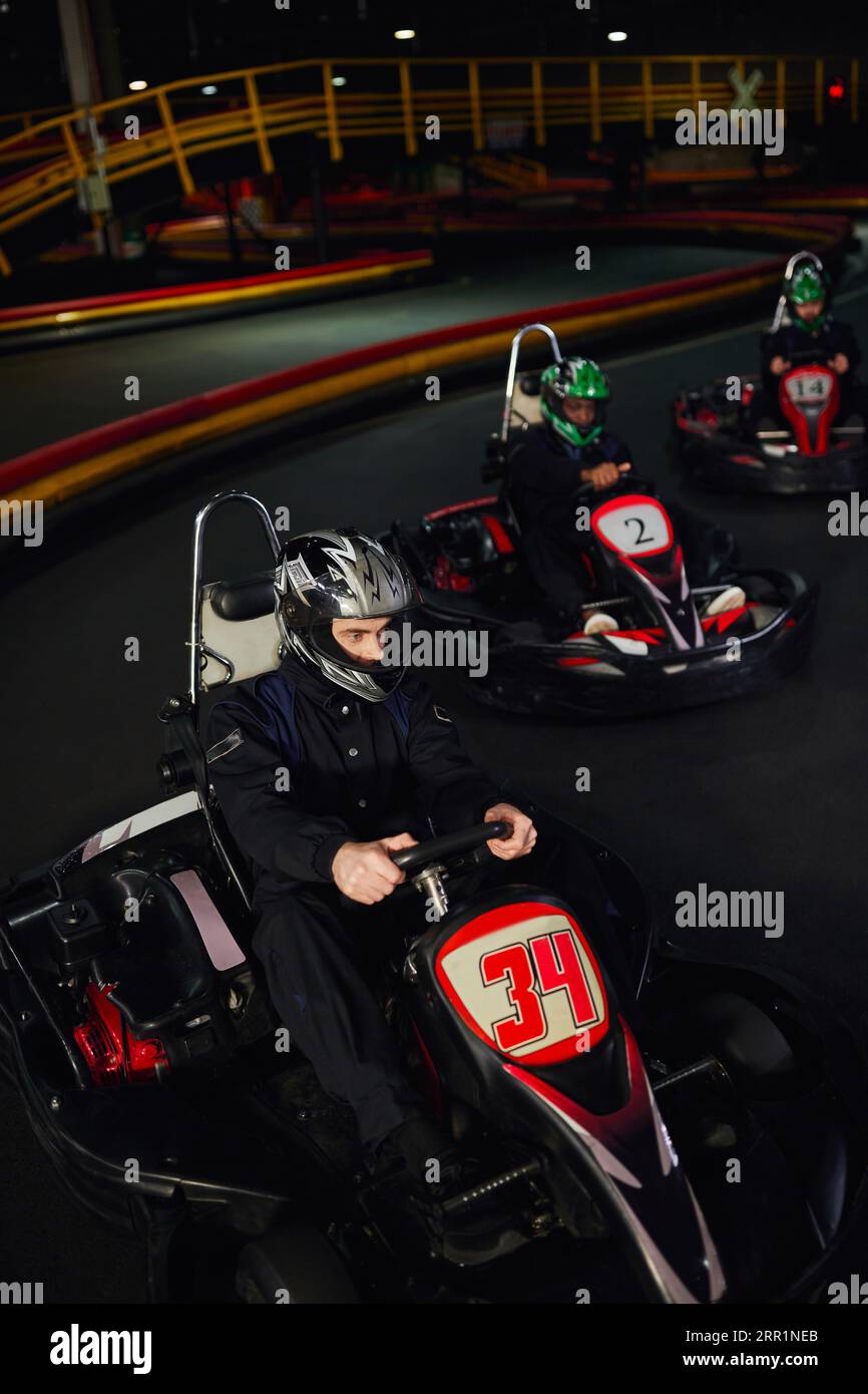 focused diverse drivers in helmets driving go kart on indoor circuit, motorsport and adrenaline Stock Photo