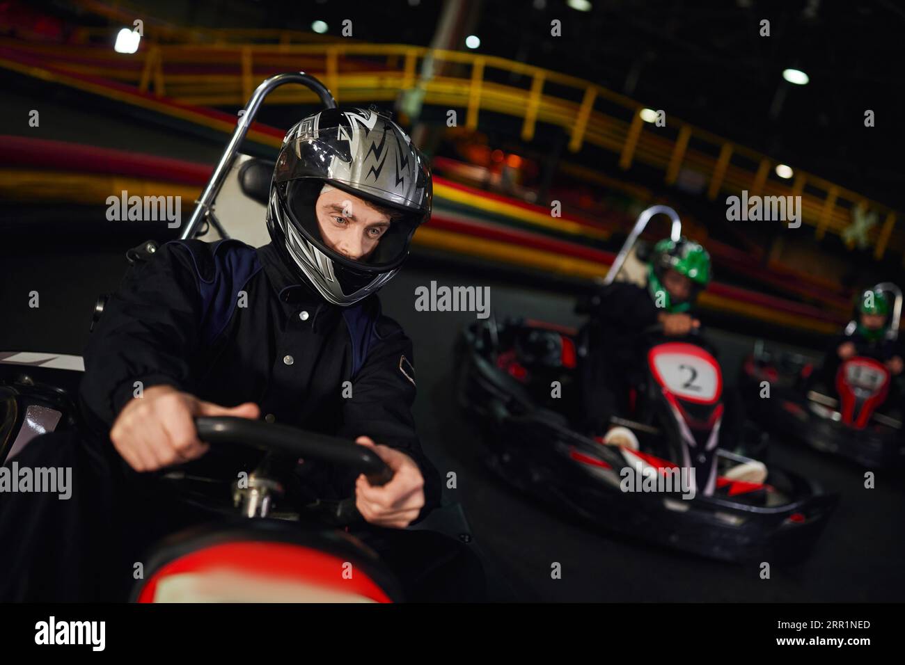 concentrated diverse men in helmets driving go kart on indoor circuit, motorsport and adrenaline Stock Photo