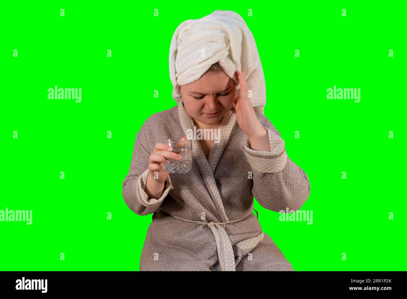 Girl with symptoms of a cold holds a glass of water in her hand on a green background (chroma key). Headache. Concept of medicine and home treatment Stock Photo
