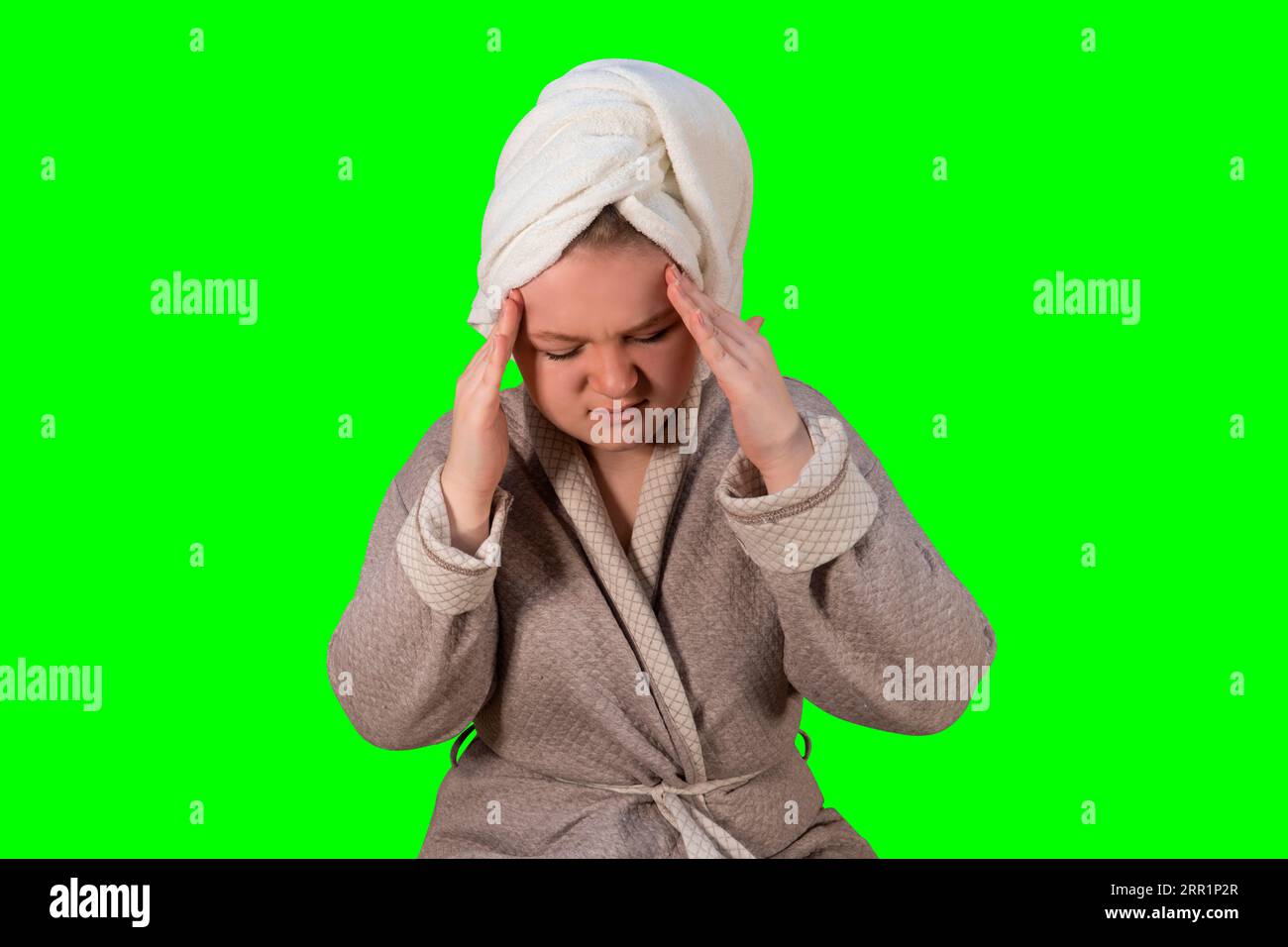 Girl in a bathrobe clasped her head in her hands on a green background (chroma key). Headache. Concept of medicine, healthcare and home treatment Stock Photo