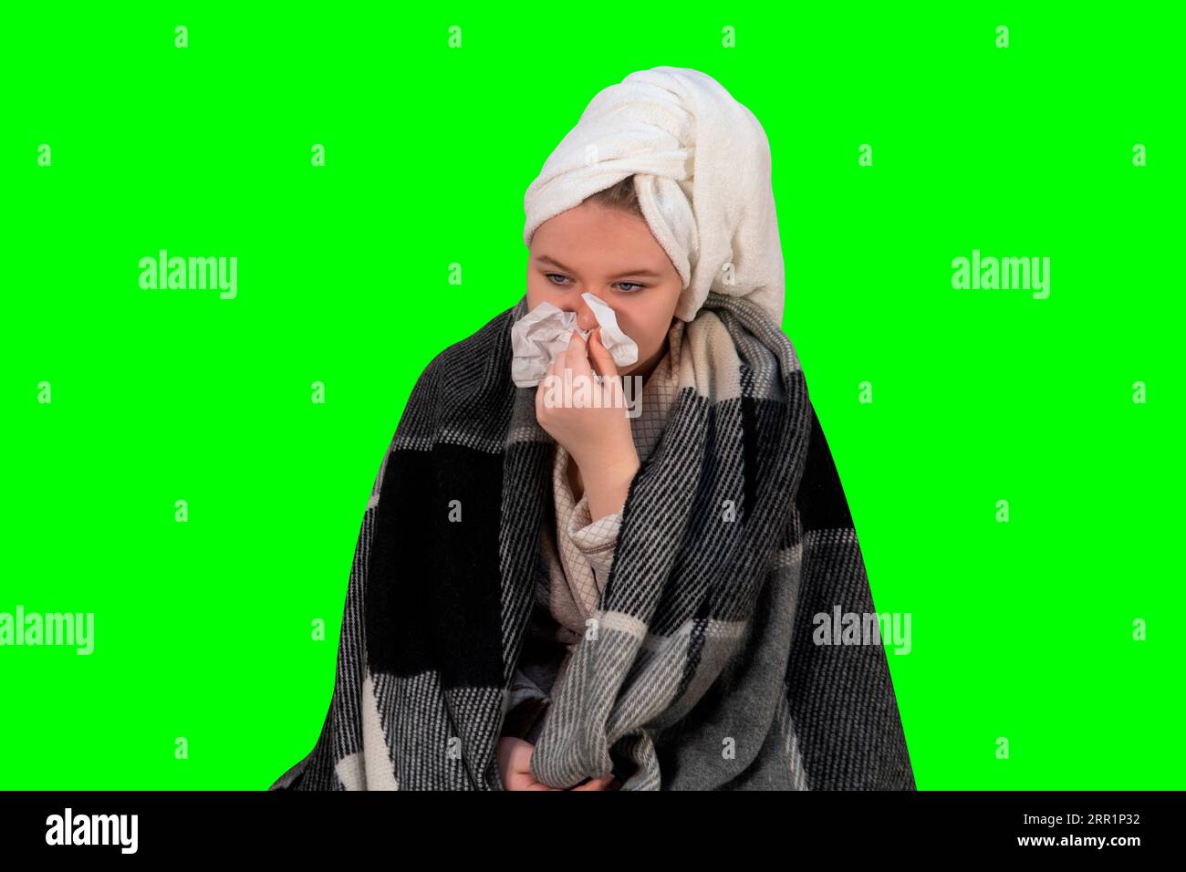 Girl with symptoms of a cold blows her nose into a paper handkerchief on a green background (chroma key). Concept of healthcare, and home treatment Stock Photo