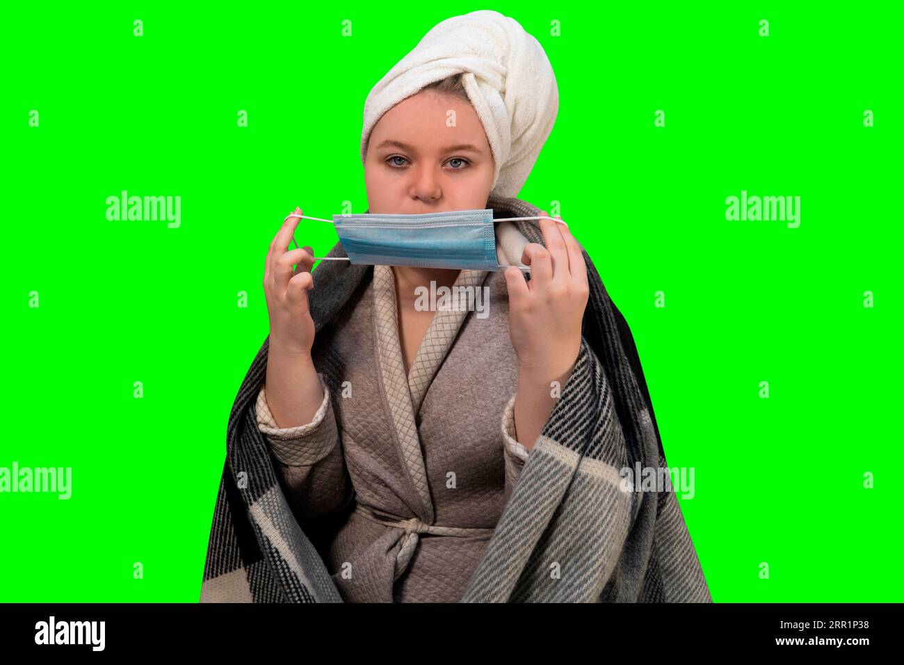 Girl with symptoms of cold puts on a protective medical mask on her face on a green background (chroma key). Concept of healthcare and home treatment Stock Photo