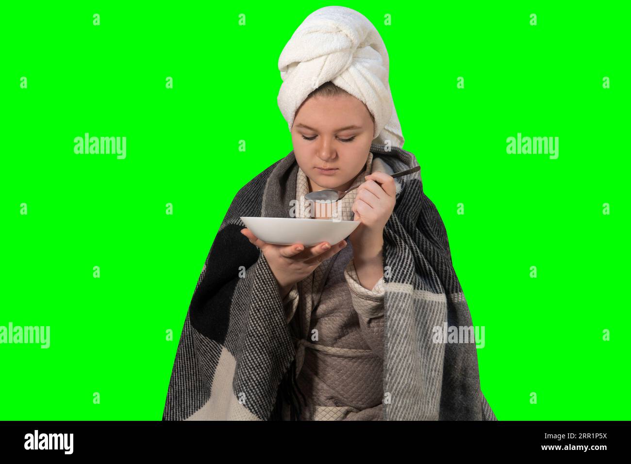 Girl with cold symptoms eats broth from a plate on a green background (chroma key). Concept of medicine, healthcare, pharmacy and home treatment Stock Photo