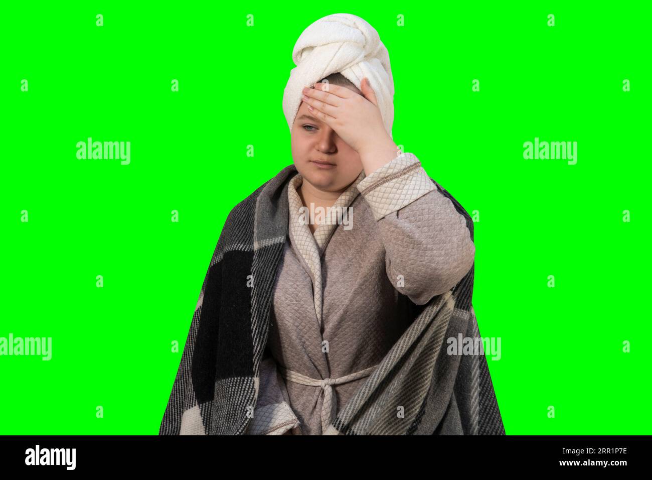 Girl with symptoms of a cold holds her head on a green background (chroma key). Headache, high body temperature. Concept of home treatment Stock Photo