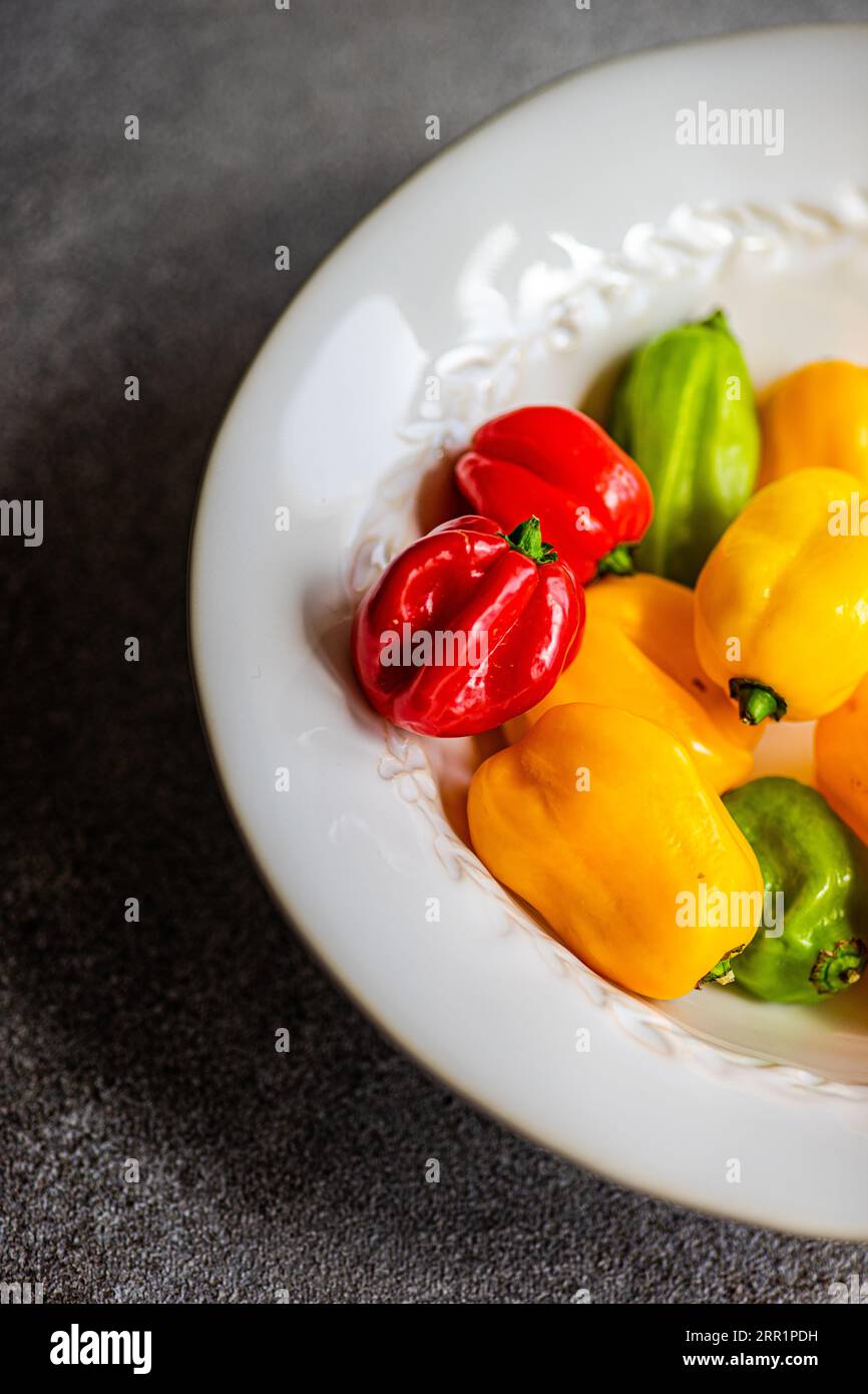 Top view of different colored peppers placed in a round white ceramic plate on a concrete background Stock Photo