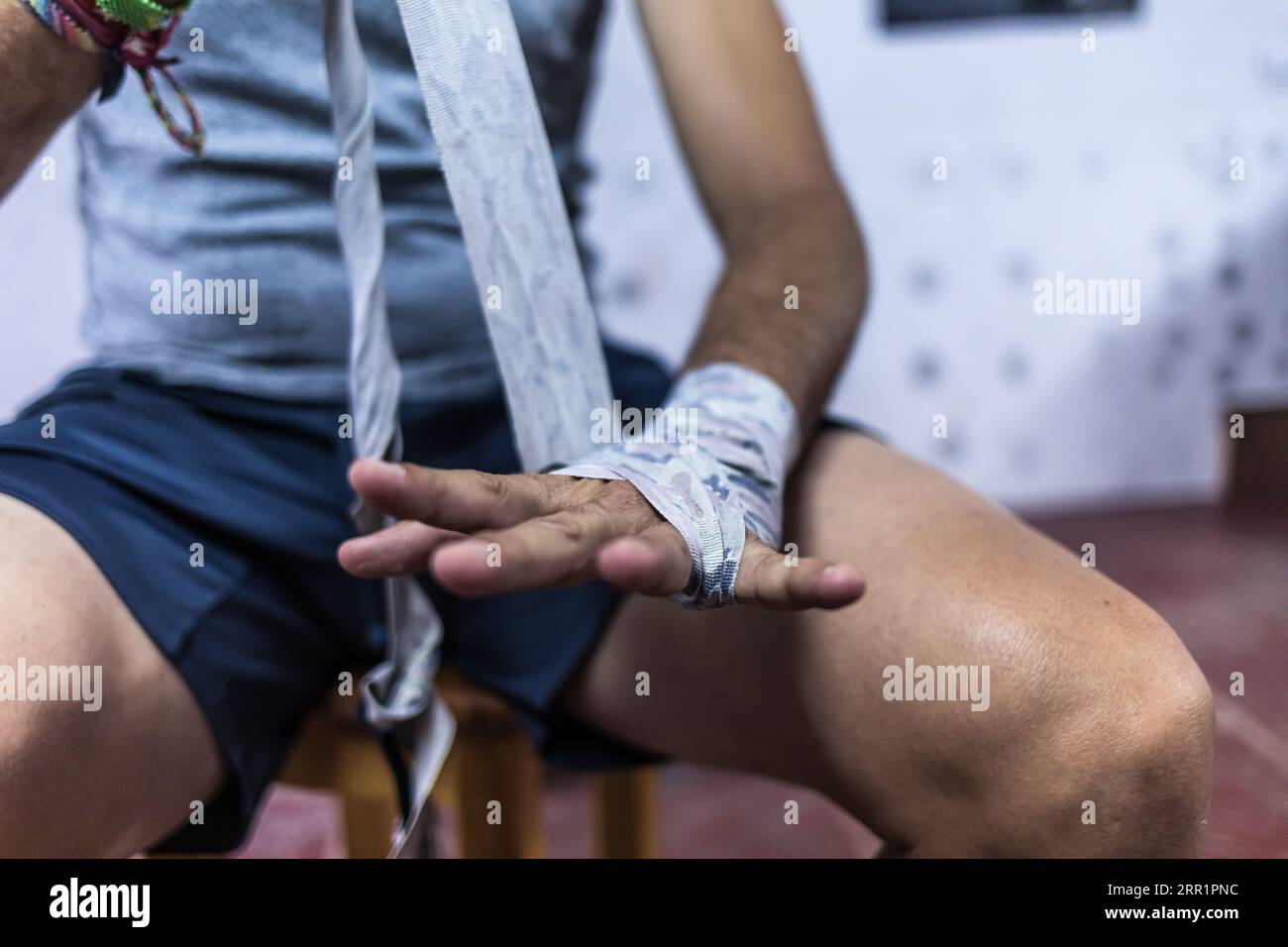 Crop anonymous male boxing athlete sitting while wrapping hand with ...