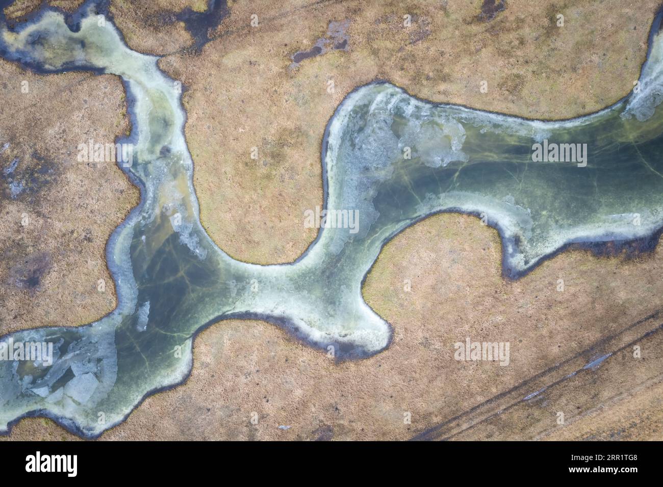 Aerial view of blue frozen meandering river water on rough brown ...