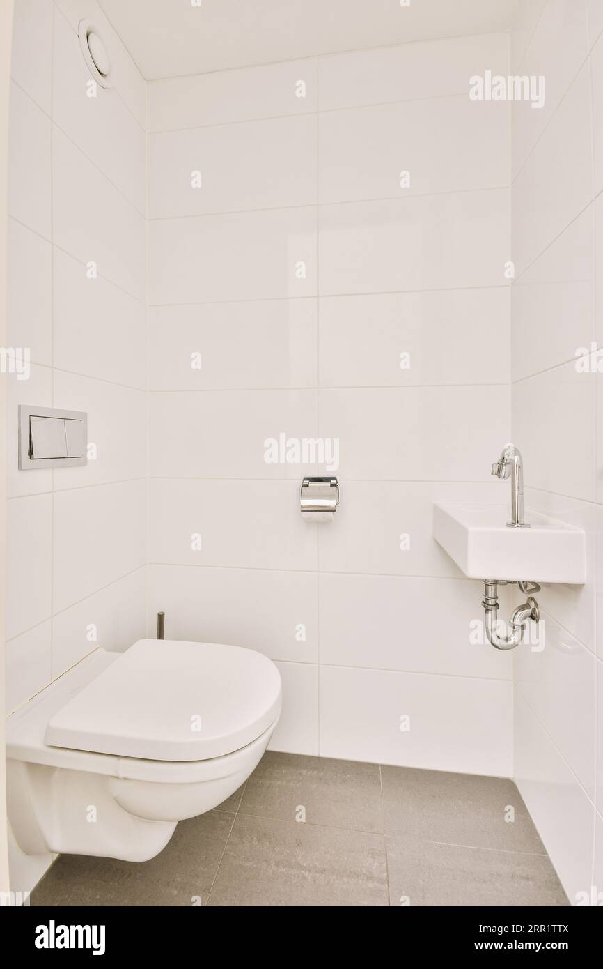 Wall hung toilet and small sink in corner in lavatory room with beige