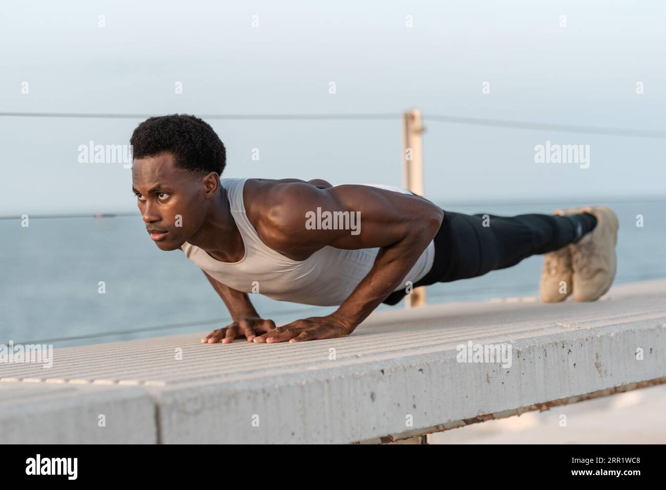 Full body of determined African American male in sportswear doing plank exercise on parapet near sea and looking forward Stock Photo Alamy