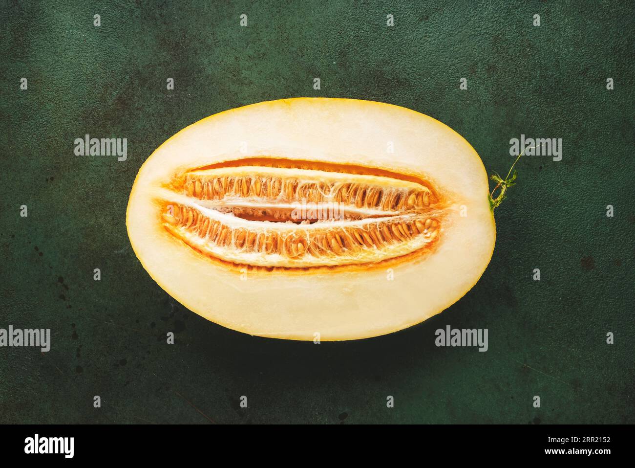 Large oval melon, cut half with seeds on rustic green background, top ...