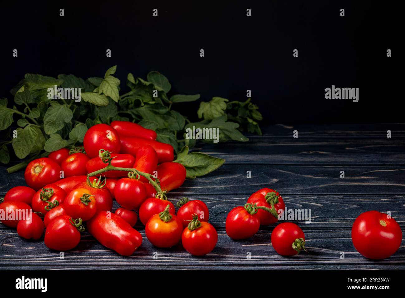 Different types of tomatoes on wood, tomato leaves, copy room, dark
