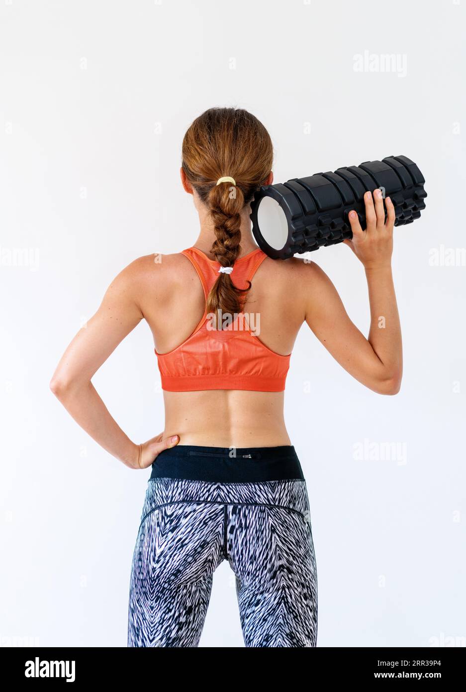 Rear view photo of female fitness coach standing in front of white background in studio with foam roller in hand. Stock Photo