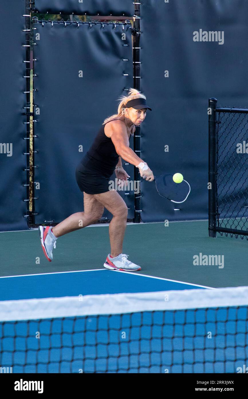 A female pickleball player returns a serve with her backhand on a