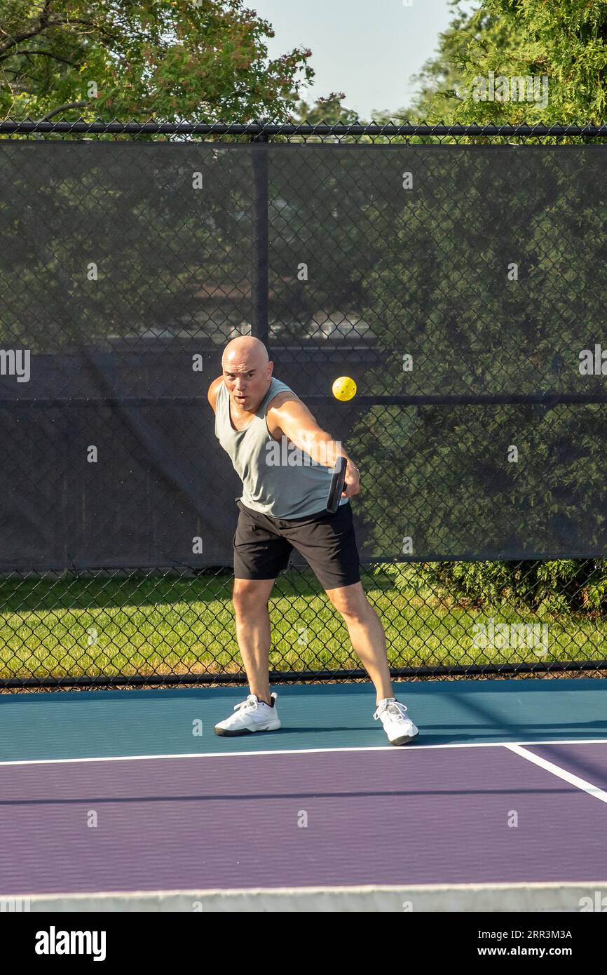 A male pickleball player returns a serve of a bright yellow ball with