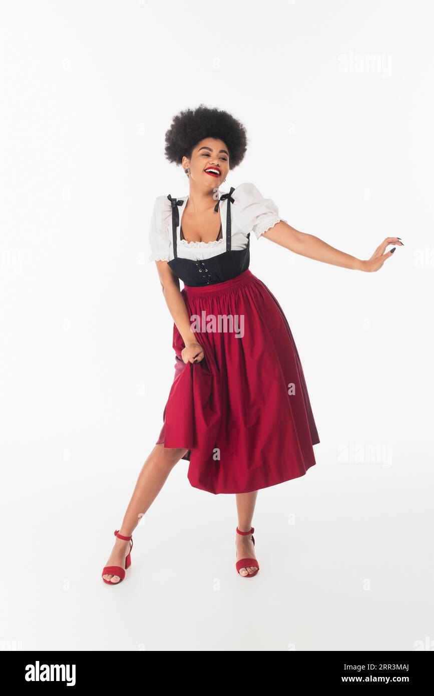 energetic african american waitress in authentic bavarian dress dancing during oktoberfest on white Stock Photo