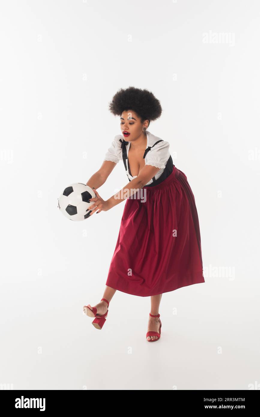 african american oktoberfest waitress in traditional bavarian dirndl playing football on white Stock Photo