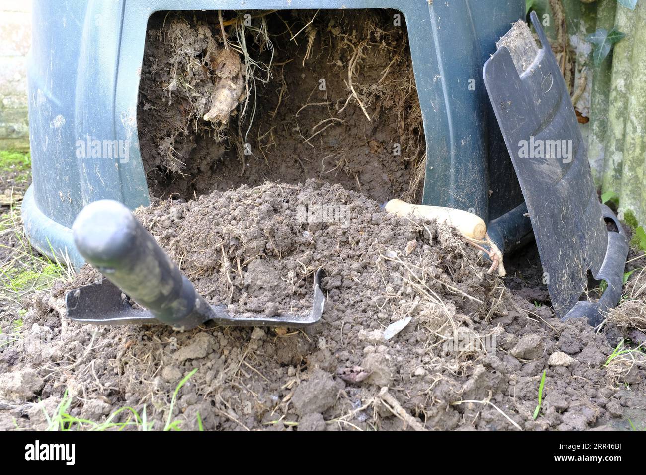 Compost bin being emptied from the bottom with the aid of a shovel and