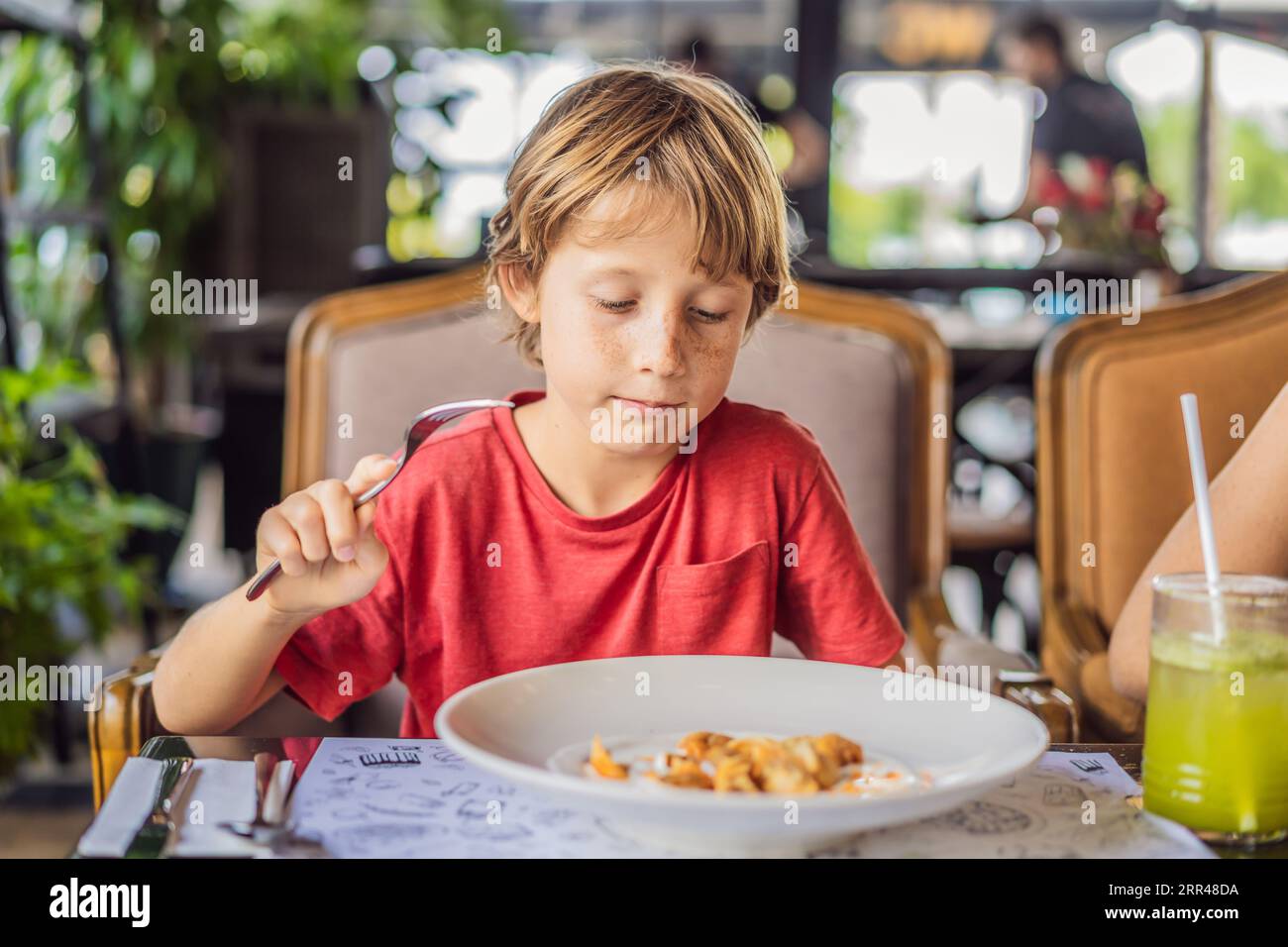 Portrait of small caucasian boy little child eating at restaurant in sunny day while sitting by the table alone - healthy eating growing up concept Stock Photo