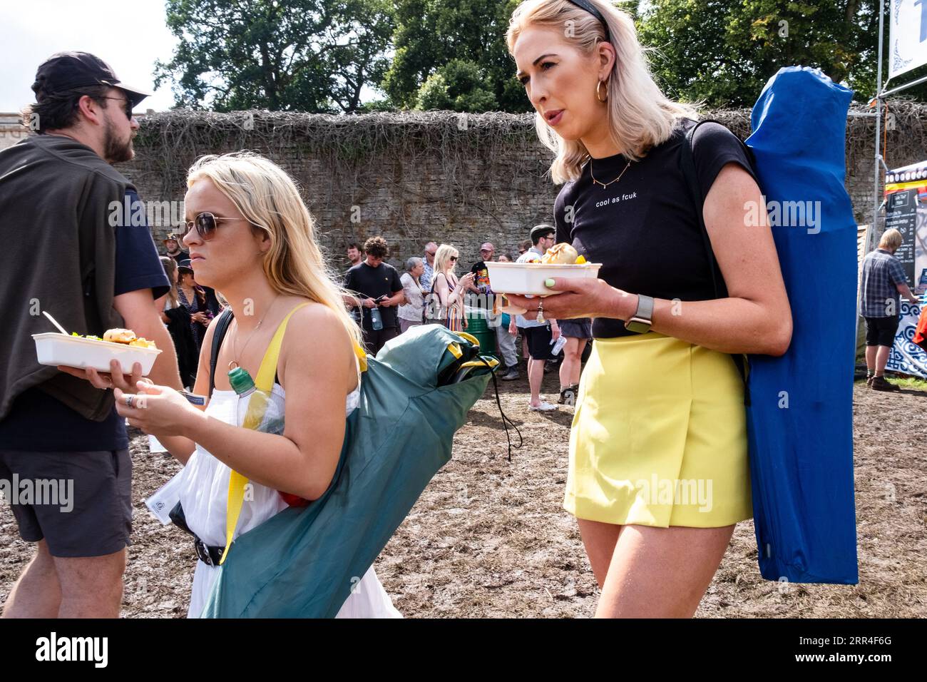 Two girl friends with takaway festival food in the muddy Walled Garden at Green Man Festival, Brecon, Wales, UK, 2023. Photo: Rob Watkins Stock Photo