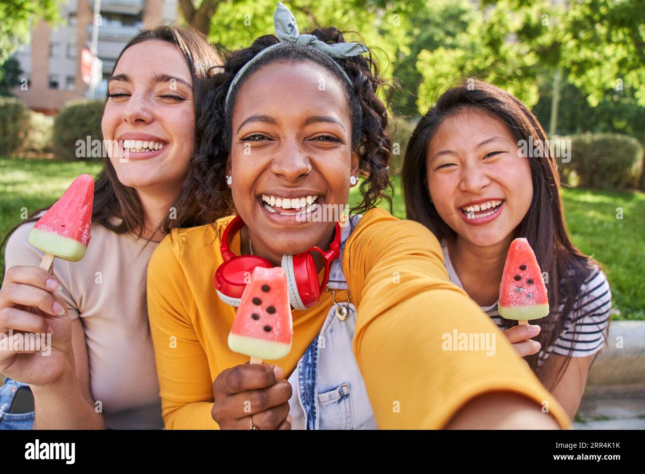 Close up faces three smiling young multi-ethnic women outdoors eating ice cream. Concept friendship. Stock Photo