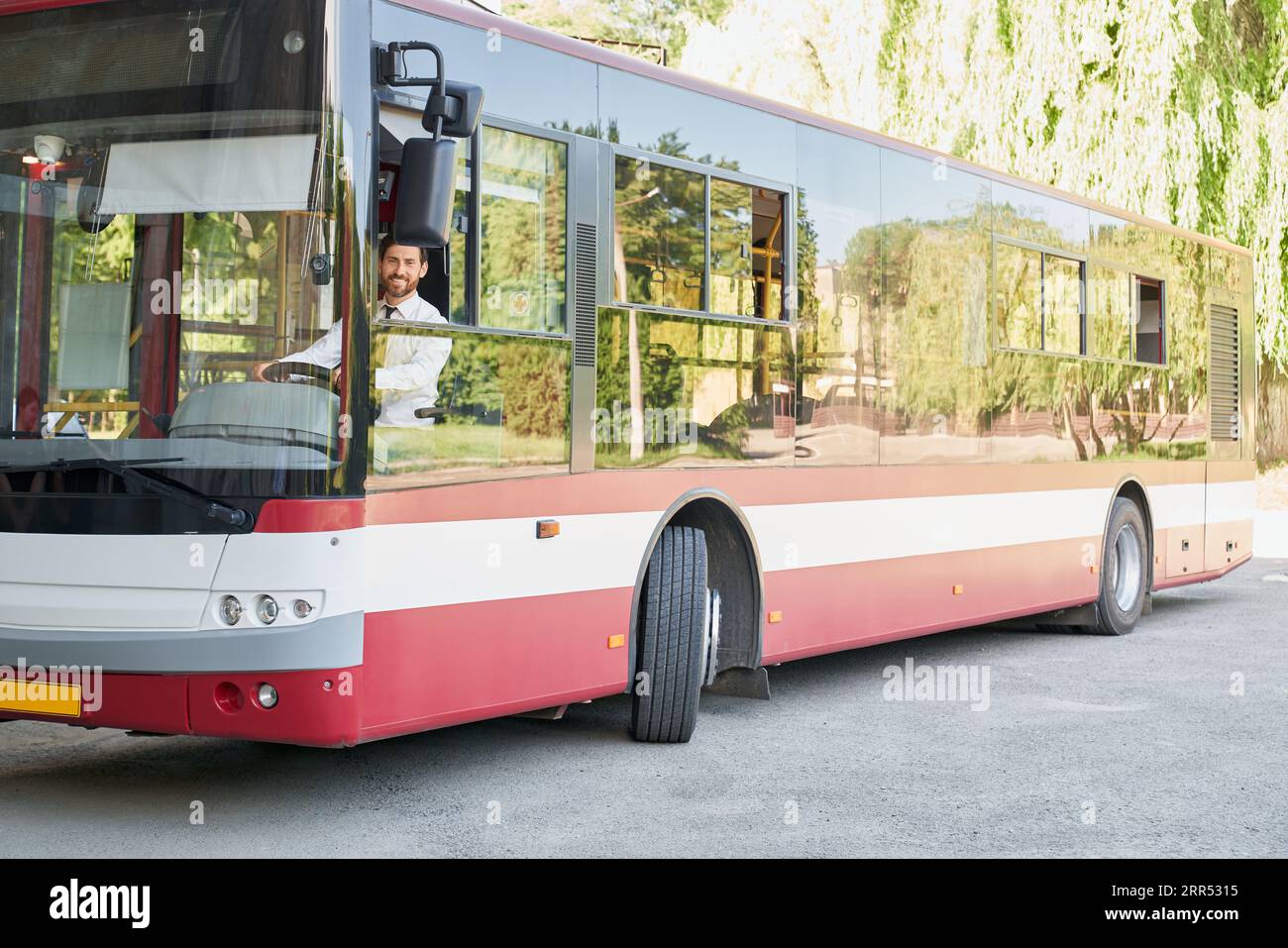 Elegant driver sitting in shuttle bus, smiling to camera at summer day
